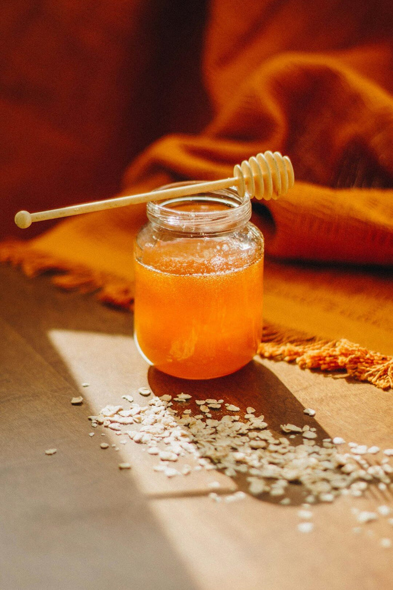 A jar of golden manuka honey with a honey dipper, showcasing manuka honey health benefits in a cozy setting.