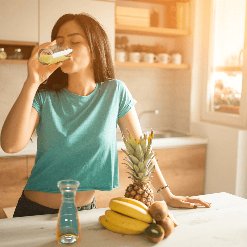How Manuka Honey Can Enhance Your Fitness Routine - woman drinking healthy juice in a kitchen with fruits