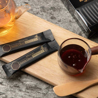 Manuka Honey MGO 300+ sachets on a wooden tray with a cup of honey and tea pot.