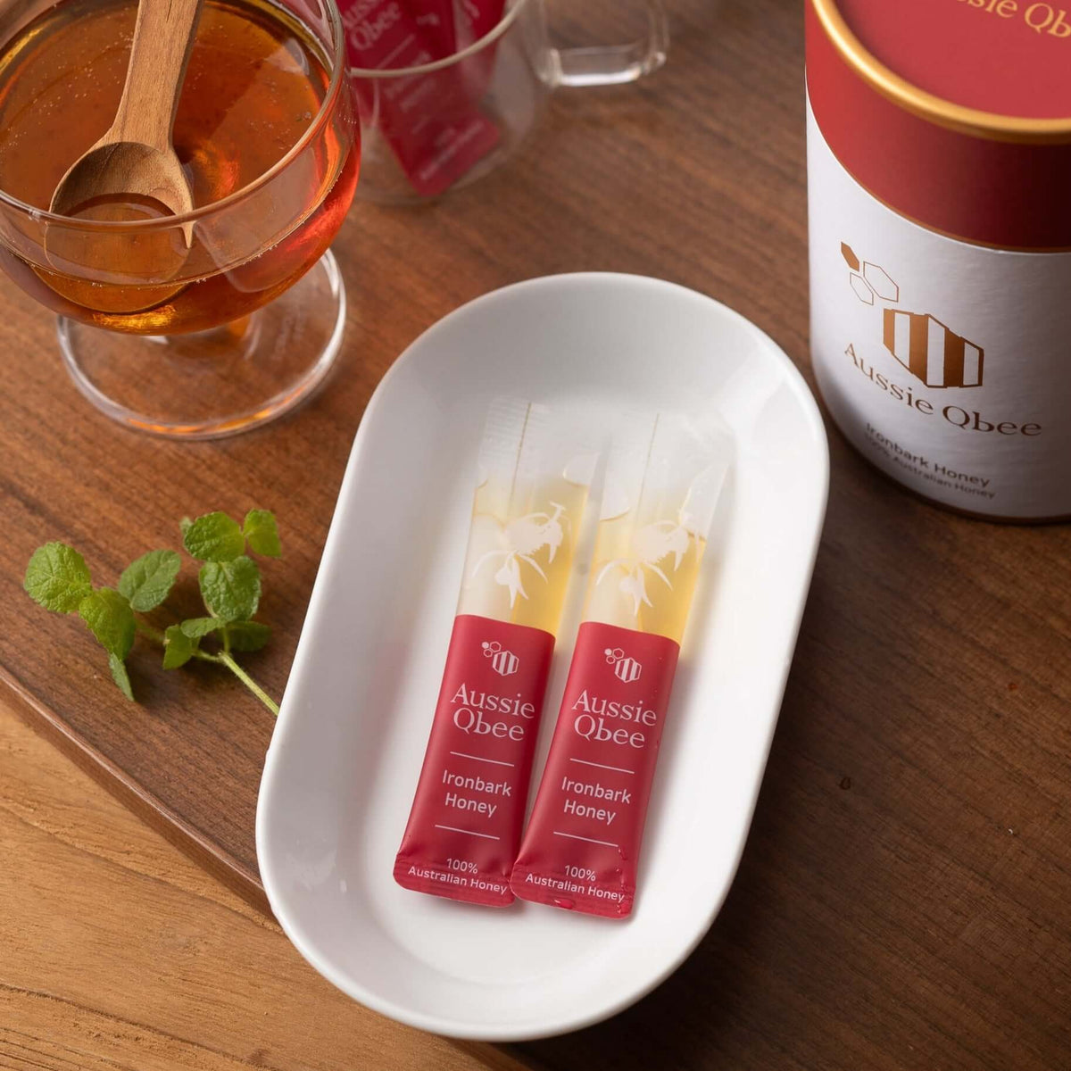 Ironbark Honey 360g sachets presented in a white dish with a glass of honey and mint leaves in the background.