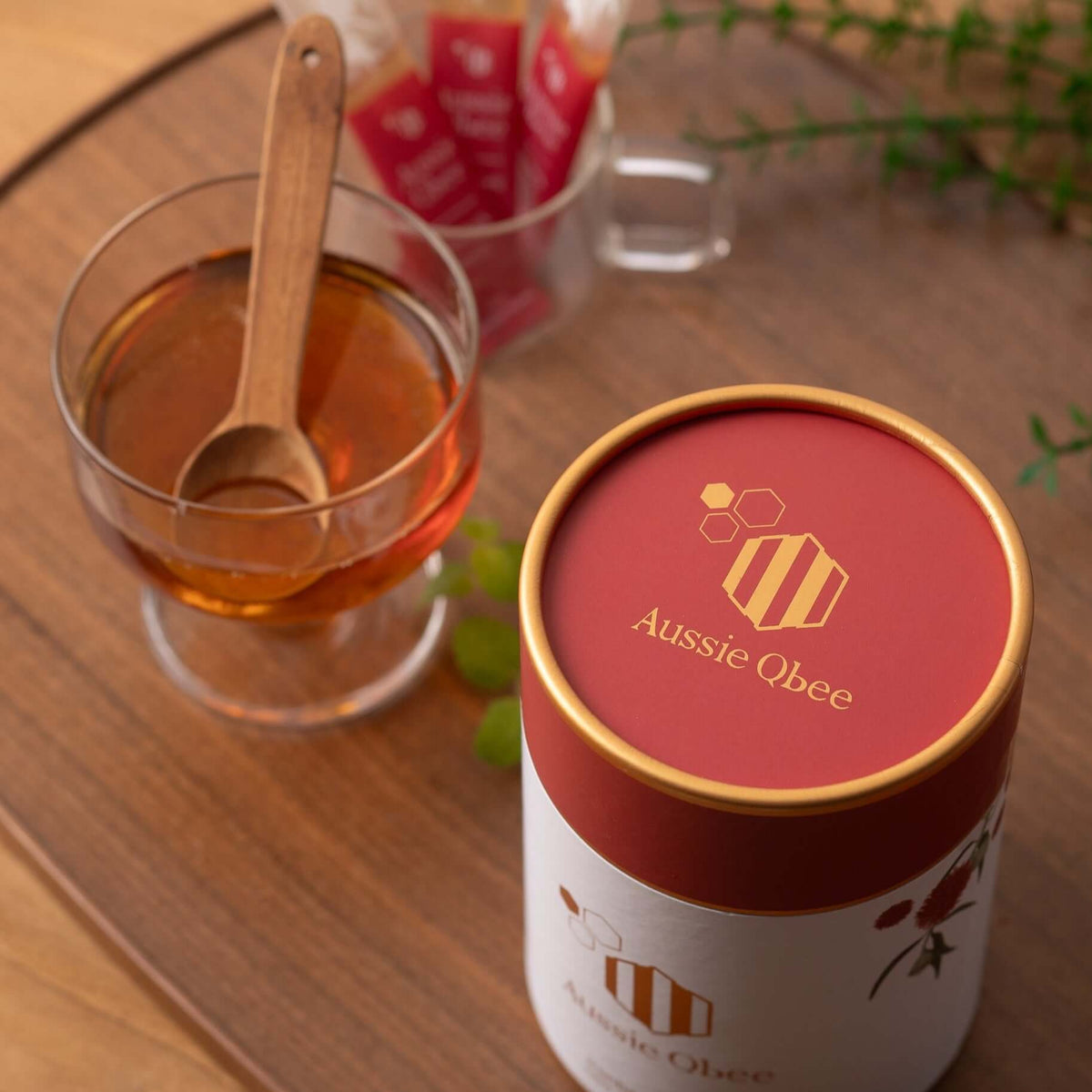 Ironbark Honey 360g from Aussie Qbee in a stylish container beside a cup of honey tea and a wooden spoon.