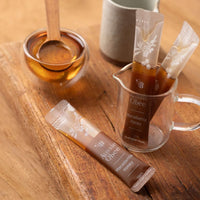 Ironbark & Macadamia Honey in packets with a honey dipper and honey jar on a wooden surface.