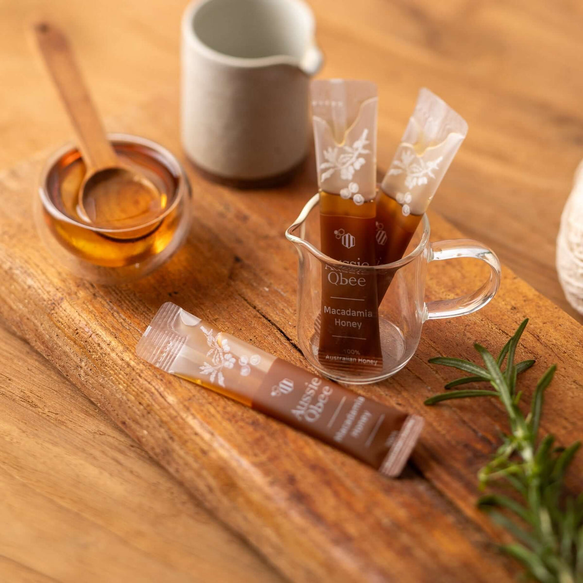 Macadamia Honey sachets in a glass container with a honey dipper and a decorative wooden board.