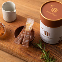 Macadamia Honey packets and jar from Aussie Obee displayed on a wooden table with a small bowl of honey.