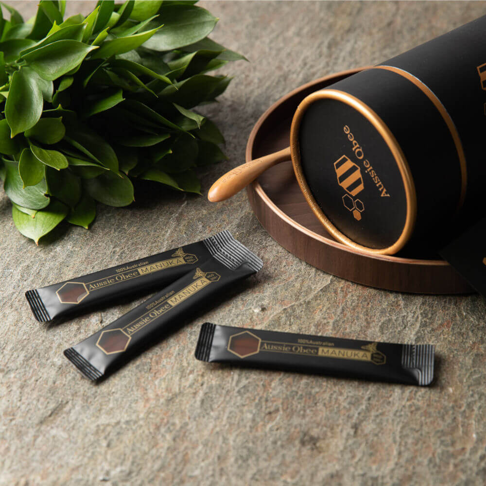 Manuka Honey MGO600+ Gift Package with individual sachets and wooden spoon on a decorative surface.