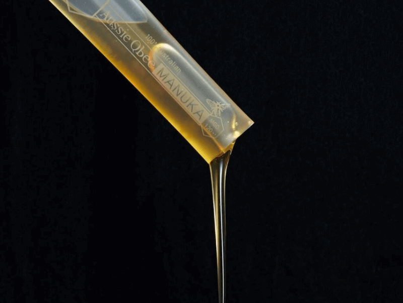Honey stick with honey dripping onto a wooden spoon against a black background