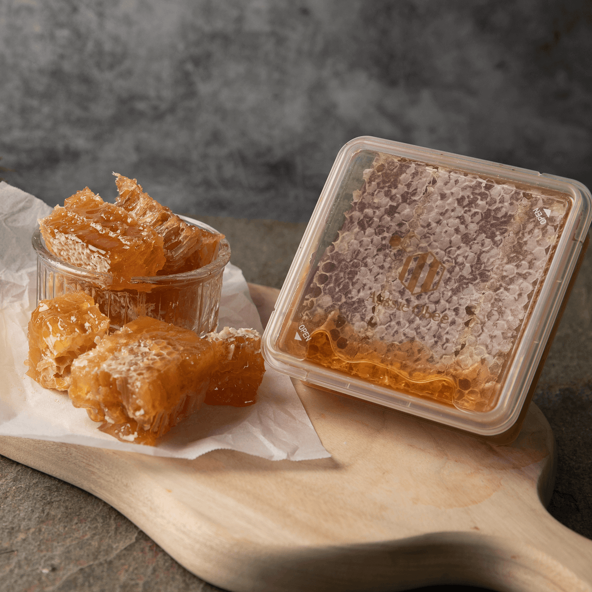 Premium Natural Honeycomb 400g displayed in a clear container with fresh honeycomb pieces on a wooden board.