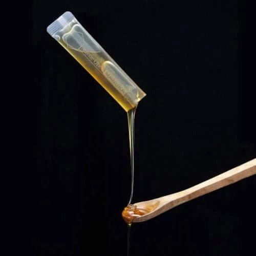 Manuka Honey MGO 150+ in a single-serve sachet pouring onto a wooden spoon, showcasing its thick, golden texture.
