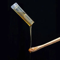 Manuka Honey MGO 150+ in a single-serve sachet pouring onto a wooden spoon, showcasing its thick, golden texture.